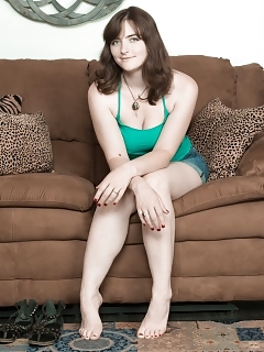 Snow Is In Her Green Top And Denim Shorts, While Lounging On Her Brown Sofa